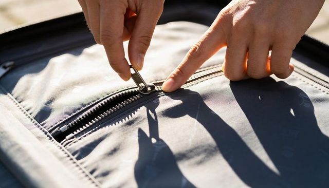 Unzipping sunlit suitcase pocket with hands pulling zipper slider and casting shadows