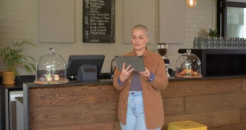 Female barista using tablet behind rustic coffee counter with pastry domes
