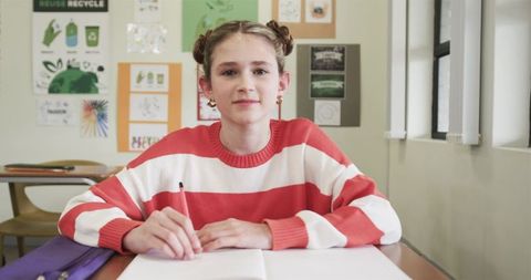 Curious Student Writing Notes in Classroom Surrounded by Educational Posters