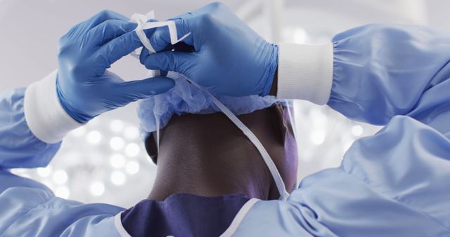 Back view of african american male surgeon in gloves tying face mask in operating theatre. Hospital, medical and healthcare services.