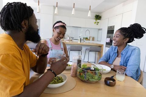 African american family sharing healthy salad and laughter in modern sunlit kitchen