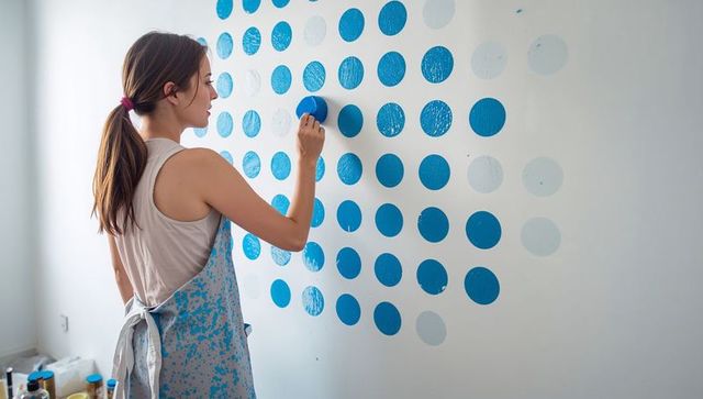 Woman painting blue dot grid on wall for diy home decor accent and geometric pattern