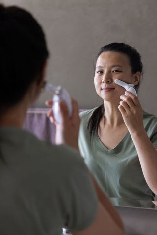 Mature african woman using facial device at bathroom mirror for gentle skincare routine