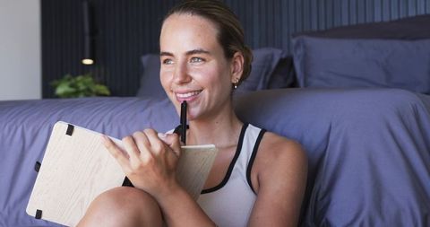 Young woman writing in notebook while sitting on bedroom floor cozy minimalist corner soft lighting