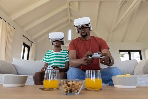 African-american father and son playing virtual reality games with controllers on couch