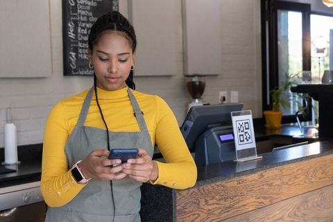 African american barista checking orders on smartphone at modern cafe counter with qr code