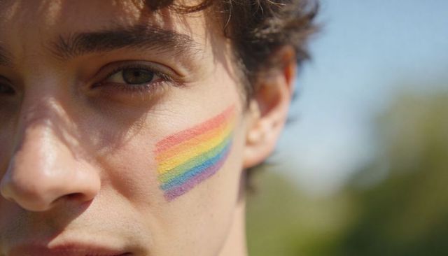 Closeup portrait of youth showing rainbow pride face paint on cheek in sunny outdoor park
