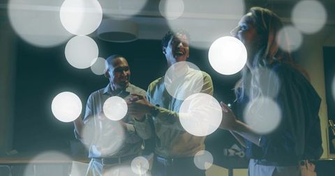 Laughing colleagues collaborating in moody office lounge with cinematic bokeh lights