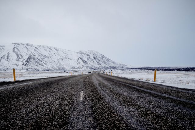 Winter road stretching out toward mountains in cold remote area. Perfect for use in travel blogs, adventure and nature articles, weather reports, or promotional materials for winter tourism destinations, capturing the serene and isolated beauty of winter landscapes.