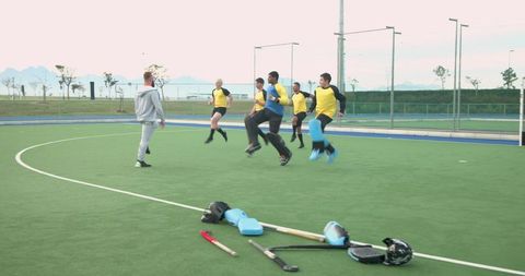 Diverse Hockey Team Practicing Jumping Drills on Turf Field Outdoors