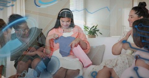 Expectant mother opening blue baby onesie at baby shower celebrating with friends and gifts