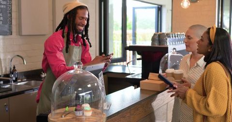 Smiling barista serving takeaway coffee to two customers at bright modern cafe counter