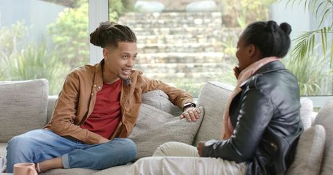 Couple having relaxed conversation on sectional sofa by window with garden view