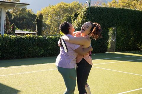 Diverse friends hugging on tennis court in sunlight