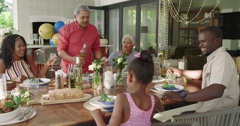Multi-generational family celebrating dinner together around wooden table with wine and bread