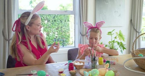 Mother and daughter painting easter eggs wearing bunny ears sharing spring craft moment