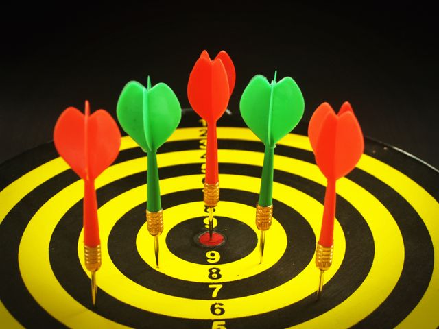 Various colored darts hitting the center of a yellow and black target board, emphasizing precision and skill. Ideal for illustrating concepts of goal achievement, competition, focus, and strategic planning in presentations, infographics, or motivational materials.