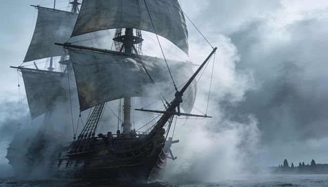 Tallship sailing through dense fog along rocky coast, square sails and weathered rigging