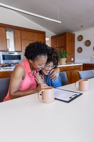 Smiling women hugging while reviewing signed paperwork at kitchen table