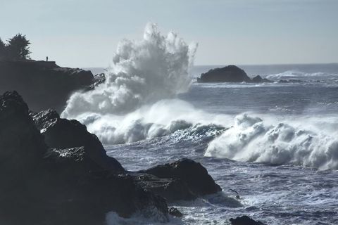 Massive Waves Crashing on Rugged Coastline with Lone Silhouette on Clifftop