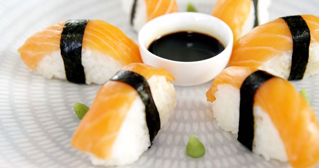 Elegant presentation of salmon nigiri sushi served with a small bowl of soy sauce and wasabi. Perfect for use in restaurant menus, food blogs, Japanese cuisine promotions, or cooking classes. Highlights the freshness and artistry in sushi preparation.