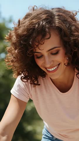 Curly woman leaning and smiling while observing object in sunny backyard vertical video