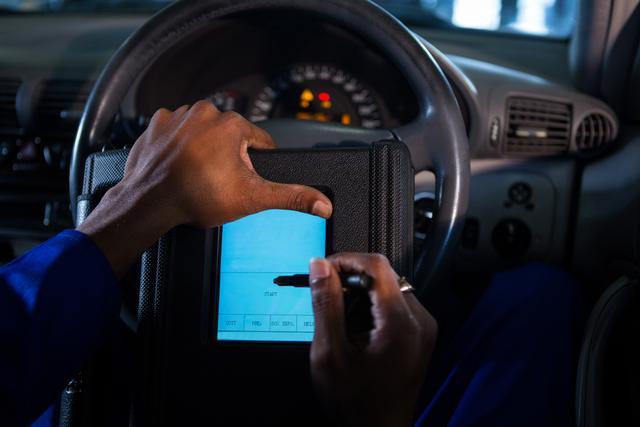 Mechanic using touchscreen device in car for diagnostics and repair. Ideal for illustrating automotive technology, modern car maintenance, and professional vehicle service.