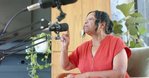 Senior african american woman recording podcast in home studio speaking into microphone