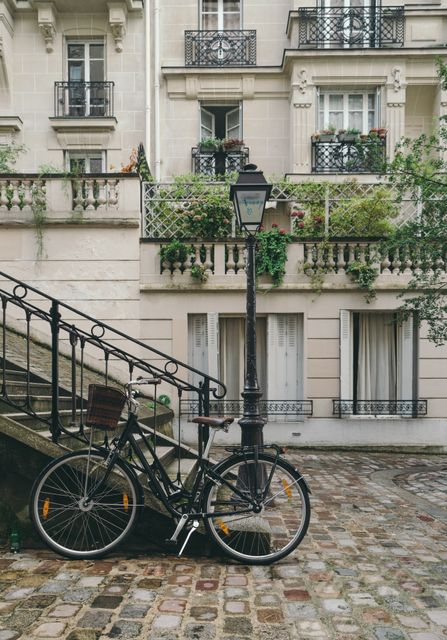 Vintage bicycle parked against stair railing on charming street with cobblestone pavement and classic European architecture in background. Perfect for travel blogs, European city guides, architectural magazines, romantic getaway promotions, historical city features.
