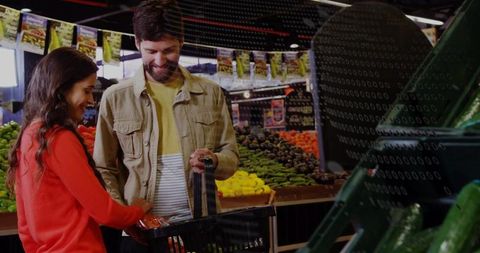 Couple choosing fresh produce in supermarket while woman showing bagged carrots