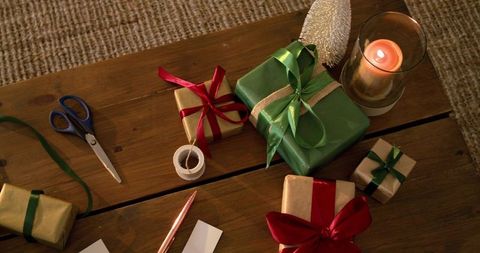 Green and gold wrapped gifts on wooden table with ribbons and candlelight, holiday decor