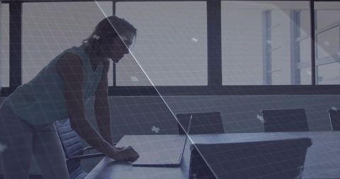 Woman leaning on table focused on laptop in conference room