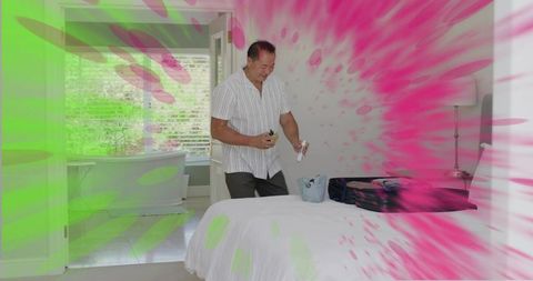 Mature man preparing toiletries, packing suitcase in minimalist bedroom with colorful splash