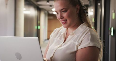 Happy professional woman using laptop in modern office hallway