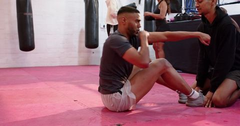 African american coach guiding athlete performing situp punches in boxing gym training