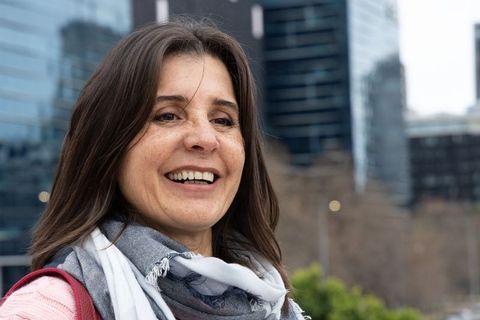 Middle-aged woman smiling on city sidewalk wearing gray scarf and pink knit sweater