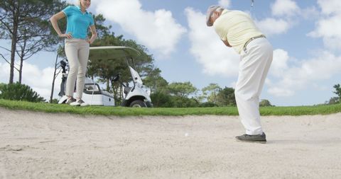 Golfers practicing bunker shots on sunny course