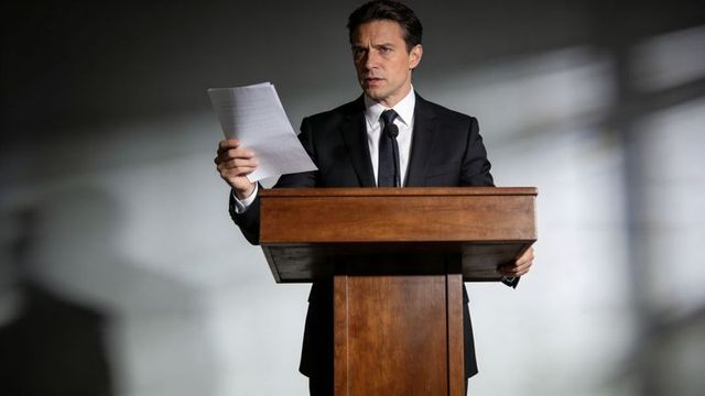 Executive delivering speech at wooden lectern under dramatic spotlight for corporate use