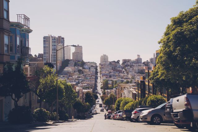 Steep urban street in San Francisco covered with parked cars, leading to distant buildings. Ideal for illustrating urban environments, city living, vibrant travel destinations, or city guide publications. Highlights hilly landscapes and residential areas with a bustling yet calm atmosphere.