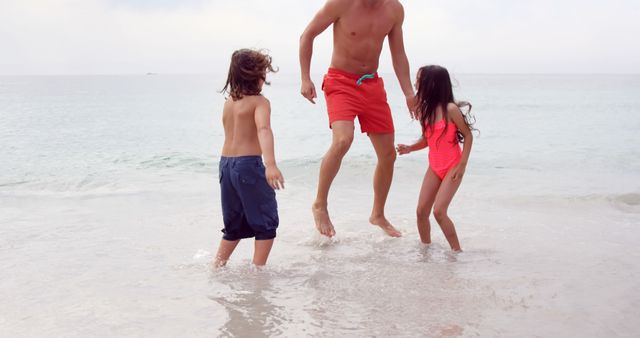 Father and two children playing in shallow ocean waves on a cloudy beach - Download Free Stock Images Pikwizard.com