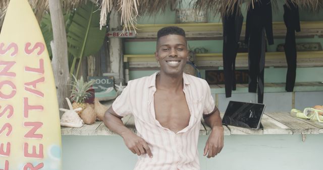Portrait of happy african american man in surf shop on beach and tablet with copy space. Lifestyle, nature, vacation, summer and leisure, unaltered.