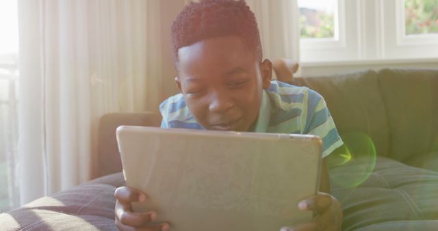 Happy african american boy lying on couch using tablet and smiling - Download Free Stock Photos Pikwizard.com