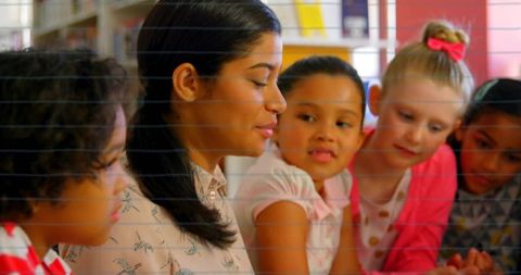 Elementary teacher guiding diverse girls during reading and storytelling in classroom library