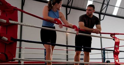 Boxers resting between rounds while trainer coaching female fighter, sparring break in gym ring