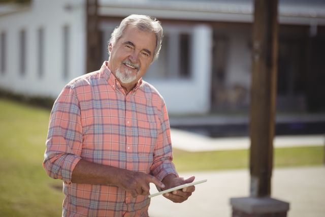Senior man enjoying a sunny day while using a digital tablet outdoors. Ideal for themes related to technology adoption among older adults, modern lifestyle, retirement activities, and promoting digital literacy among seniors.