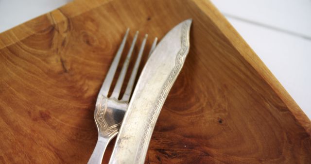 A fork and knife rest on a wooden plate, with copy space. The utensils are positioned close together, suggesting a pause between courses or the end of a meal.