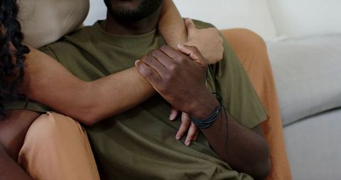 Couple embracing on sofa holding hands closeup for cozy home romance wellness