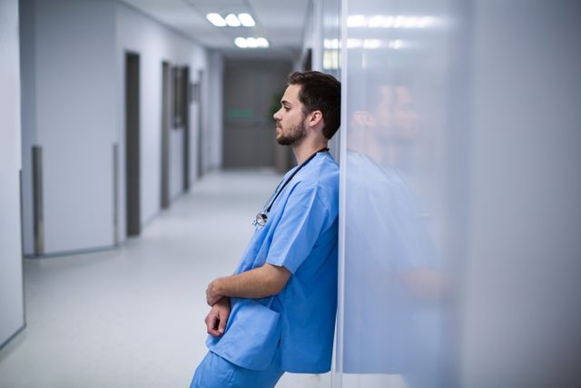 Tensed male nurse leaning on wall in corridor of hospital
