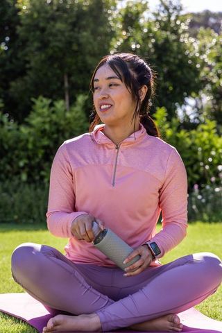 African american asian woman practicing outdoor yoga on pink mat wearing activewear