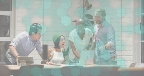 Huddling team collaborating around laptop with teal hex overlay in modern office